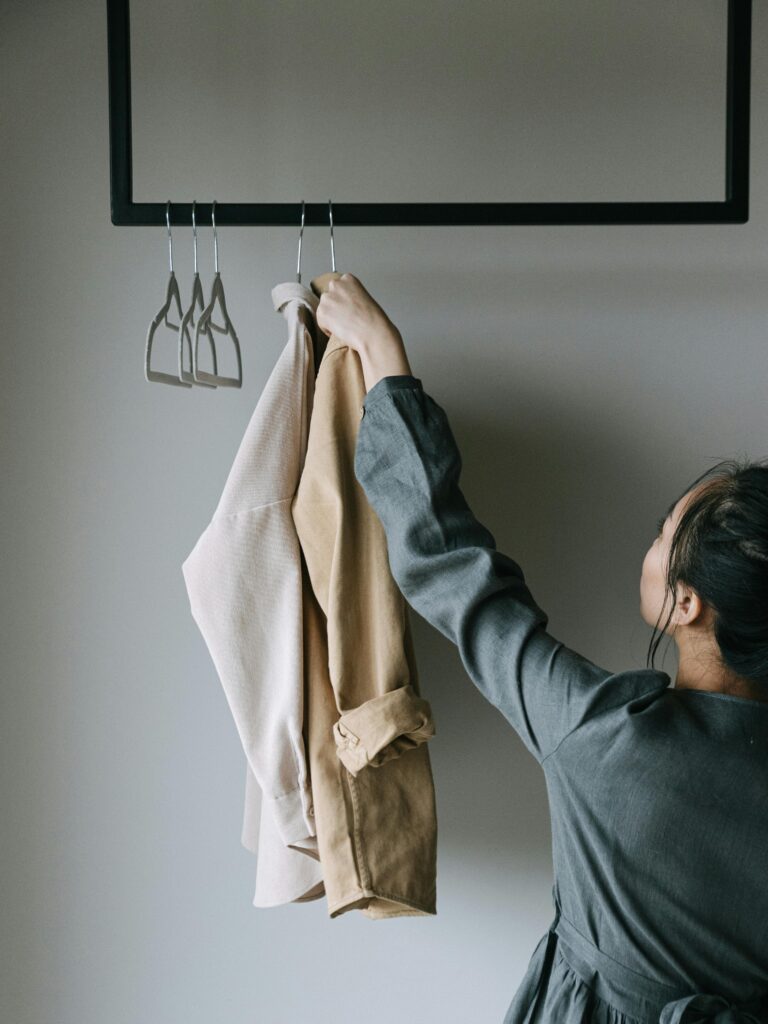 A woman arranges coats on a clothes rack indoors. Minimalist style.